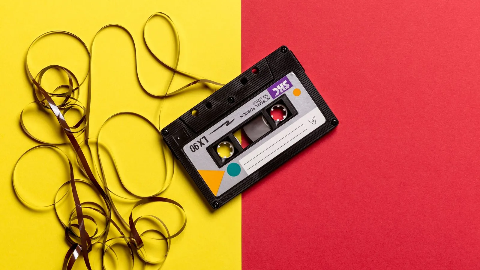 Black cassette tape with spilled magnetic tape on yellow and red background