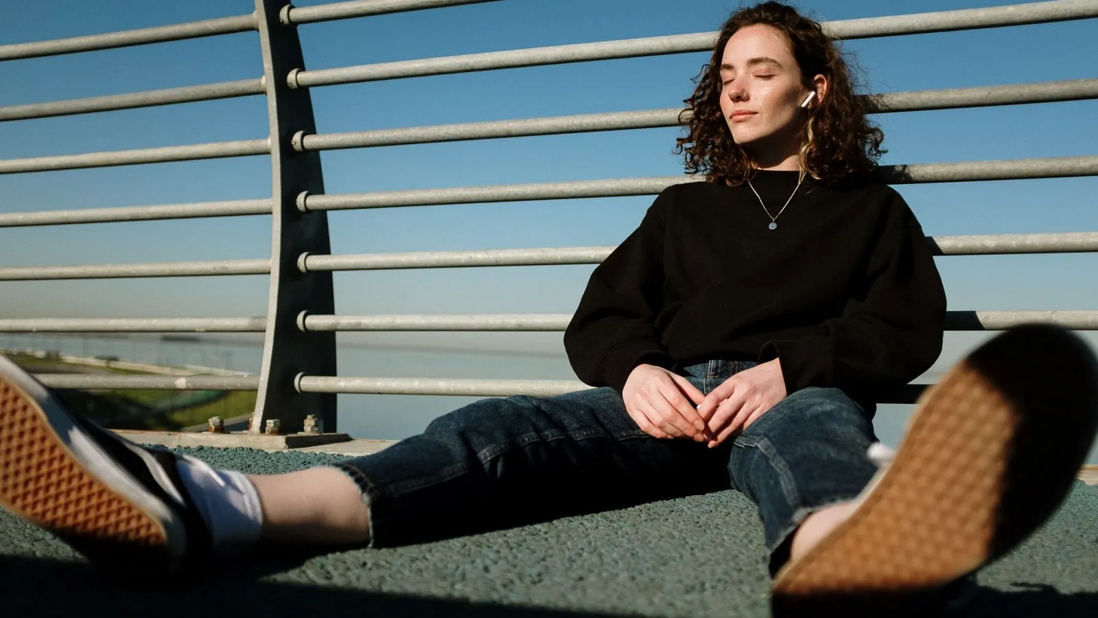 Person sitting outdoors listening with wireless earbuds against a railing